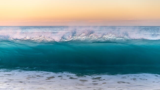 Photograph of a clear blue wave and a yellow/orange sky 
